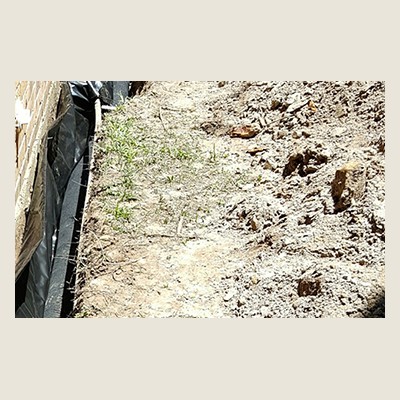 Drainage A narrow path beside a construction site with soil and sparse grass, partially covered by plastic sheeting on the left.