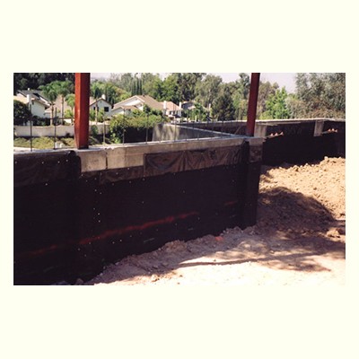 A partially constructed concrete wall with metal beams surrounded by dirt and residential houses in the background. Below Grade Waterproofing San Diego