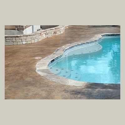 Pool Deck Coating Brown textured concrete pool deck with a curved pool featuring light blue water and stone edging.